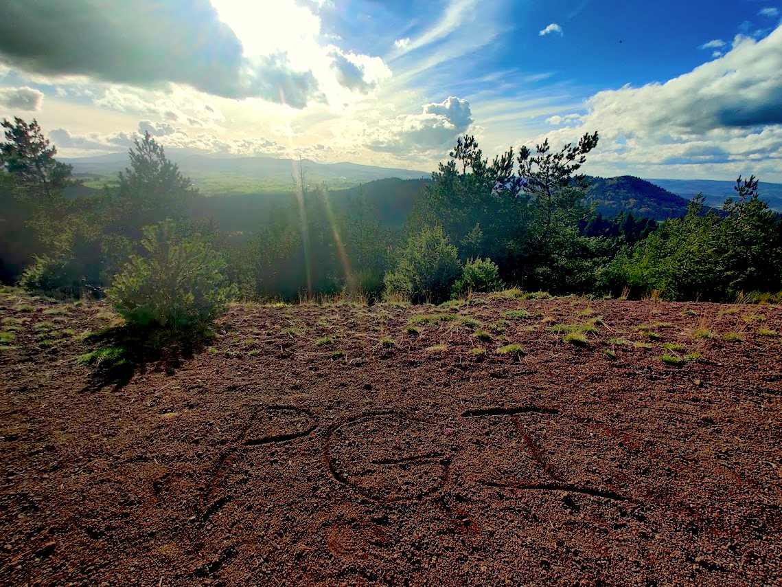 View over forested hills from a hilltop at sunset, with shapes drawn in the red soil